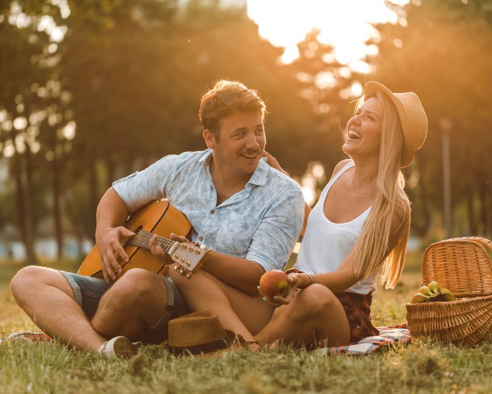 a man and woman sitting in parking laughing and man playing  a guitar