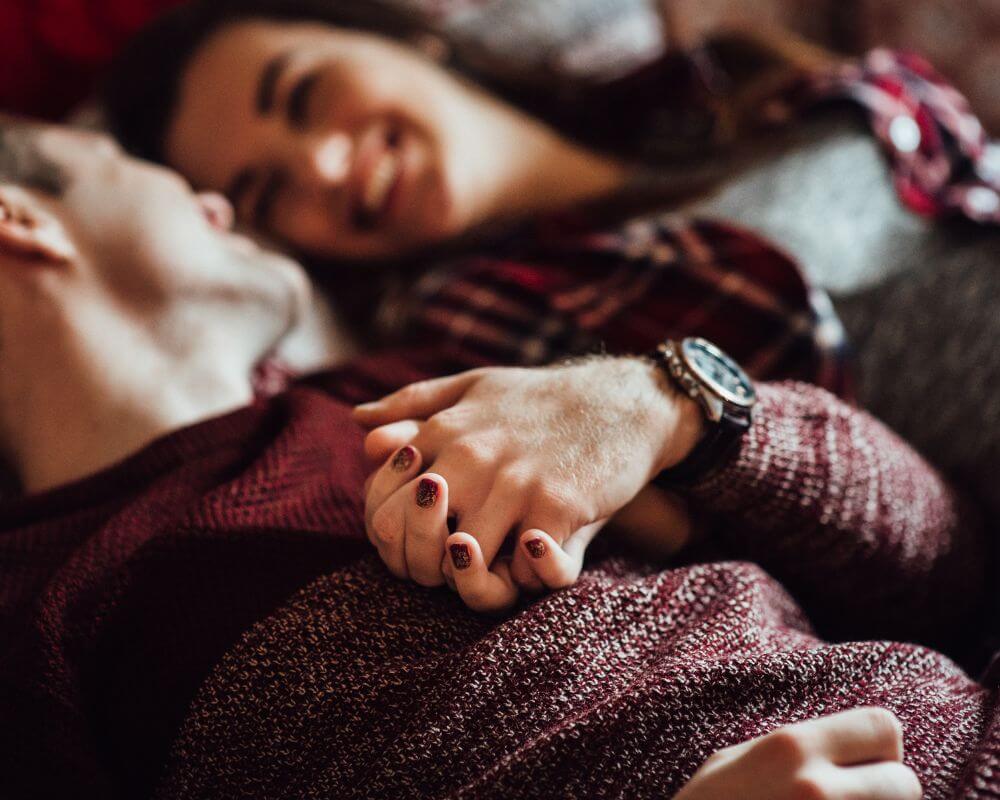 a couple intimately laying in bed with hands held together