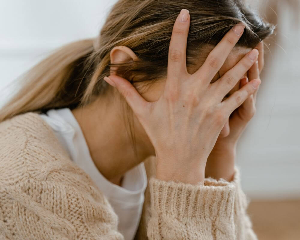 a woman frustratingly sits with hands on her head 